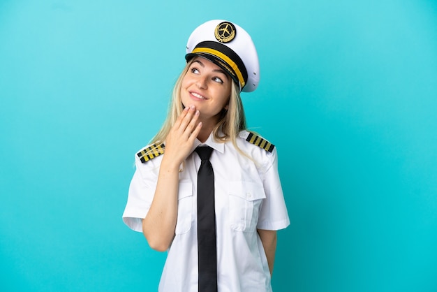 Pilota di aeroplano su sfondo blu isolato guardando in alto mentre sorride