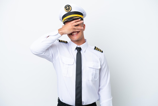 Pilota di aeroplano uomo caucasico isolato su sfondo bianco che copre gli occhi con le mani e sorridente