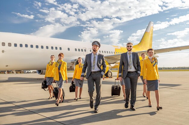 Piloti e hostess che camminano lungo l'aerodromo sotto il cielo nuvoloso