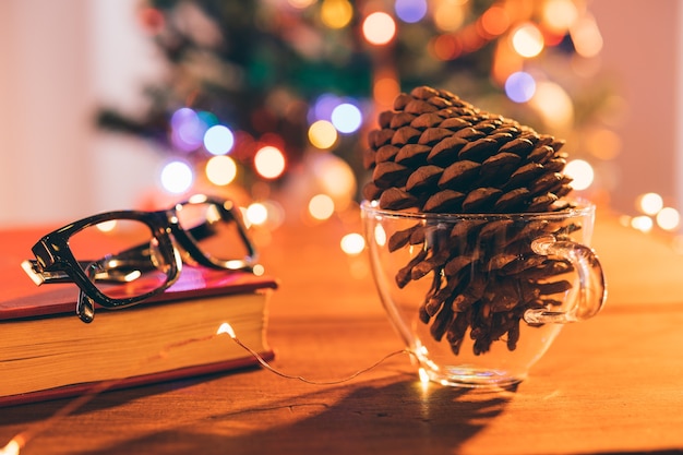 Pinecone in una tazza sul fondo vago delle luci di Natale