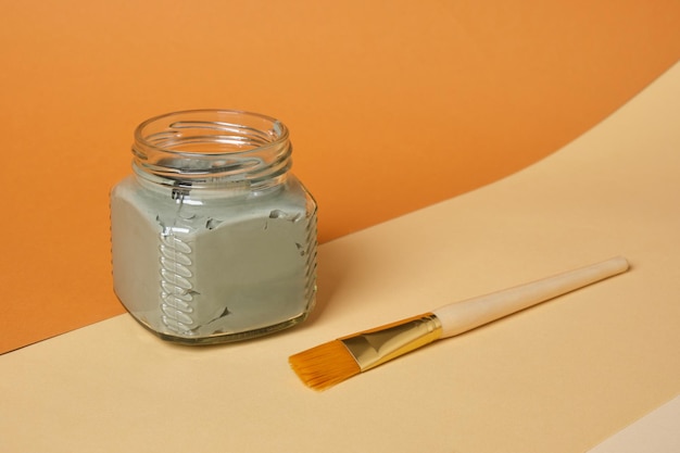 Pinta l'argilla cosmetica in un barattolo di vetro su un supporto di legno a sfondo beige e marrone