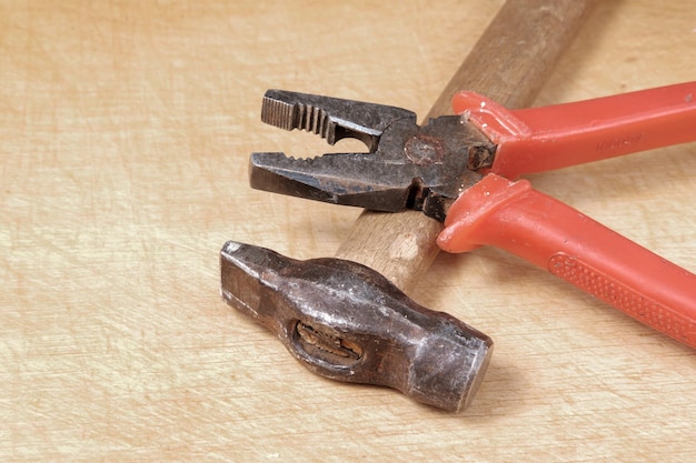 Pinze arrugginite con avvolgimento rosso giacciono su un martello con punta in metallo e manico in legno