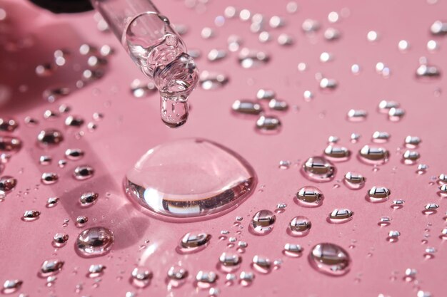 Pipetta a goccia e spruzzi di acqua micellare su uno sfondo rosa