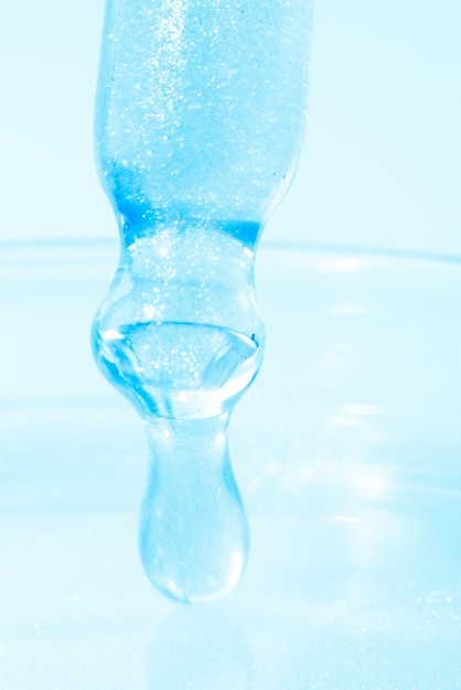 Pipetta con liquido blu gocciolante o liquido blu Primo piano su sfondo blu Chimica di laboratorio medicina Ricerca cosmetica brillantezza