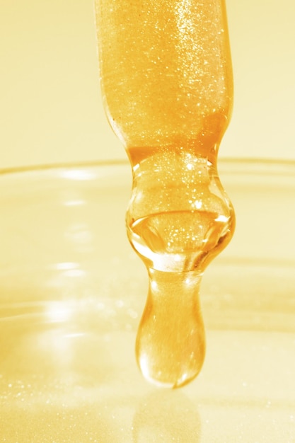 Pipetta con liquido giallo gocciolante O oro liquido Primo piano Su uno sfondo dorato Chimica di laboratorio medicina Ricerca cosmetica brillantezza