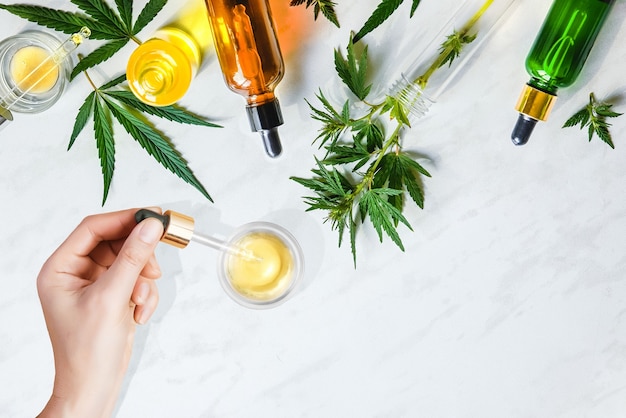 Pipetta con olio cosmetico CBD in mani femminili con cosmetici, crema di cannabis e foglie di marijuana