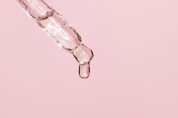 Pipetta cosmetica con liquido gocciolante e gocce su sfondo rosa siero siero gel vitamina acqua olio