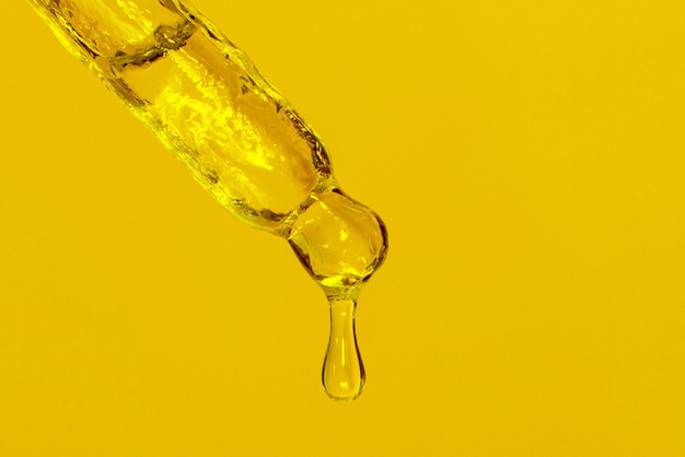 Pipetta cosmetica con olio liquido gocciolante e gocce su sfondo giallo siero siero gel vitamina acqua olio