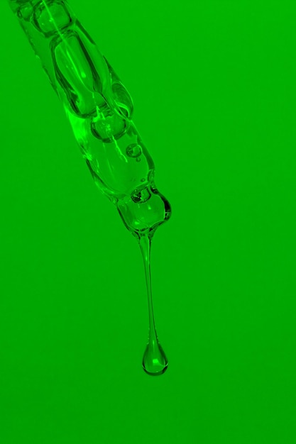 Pipetta cosmetica con olio liquido gocciolante e gocce su sfondo verde siero siero gel vitamina acqua olio Cosmetici naturali