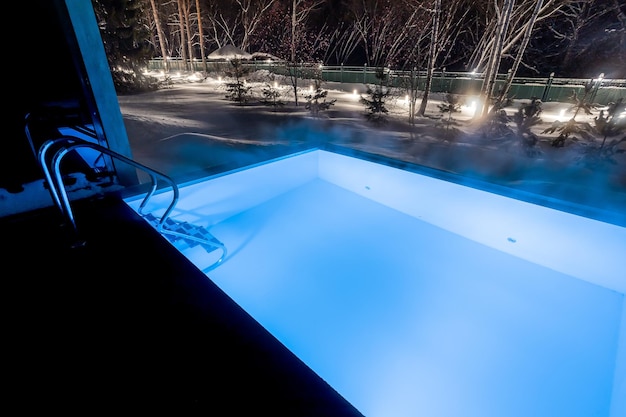 Piscina calda all'aperto con acqua blu e bagno russo in legno di notte d'inverno