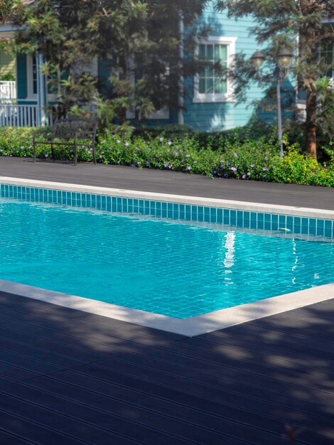 Piscina con acqua limpida e pulita, stile verticale, nessuno. Piscina di forma quadrata con piastrelle blu sui ponti di legno vicino al giardino e alla casa, senza persone. Sfondo estivo.