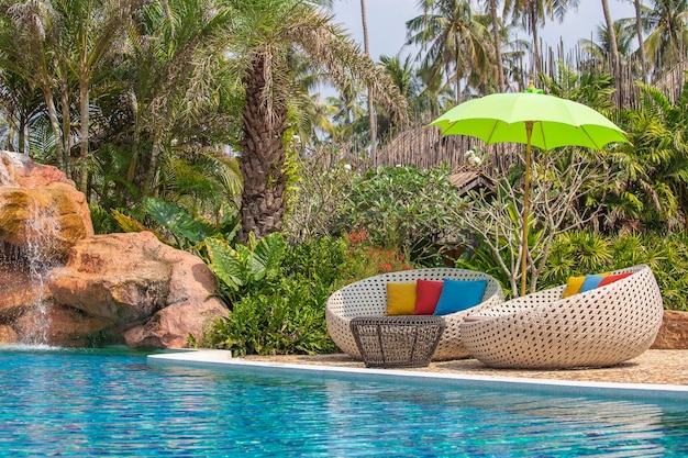 Piscina con lettini rilassanti e ombrellone in giardino tropicale in Thailandia