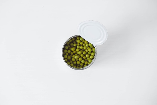 Piselli dolci verdi in scatola in una lattina di metallo di alluminio aperta su un tavolo bianco