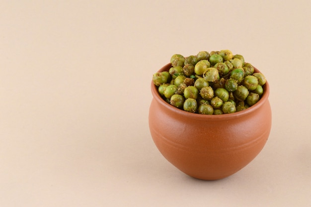 Piselli fritti speziati {chatpata matar} Spuntino indiano. Piselli verdi salati secchi in pentola di terracotta.