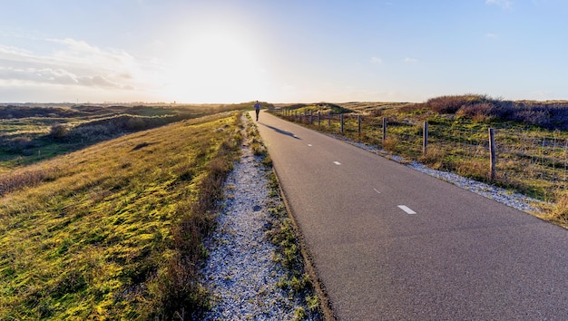 Pista ciclabile nel paesaggio delle dune con corridore all'orizzonte