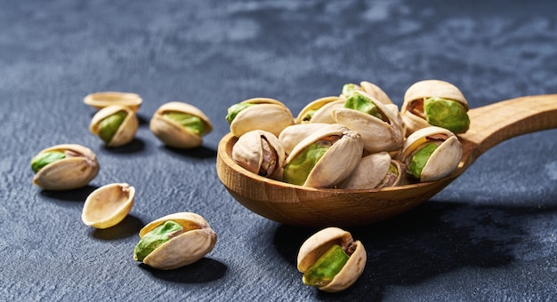 Pistacchi in cucchiaio di legno sulla tavola nera, primo piano.