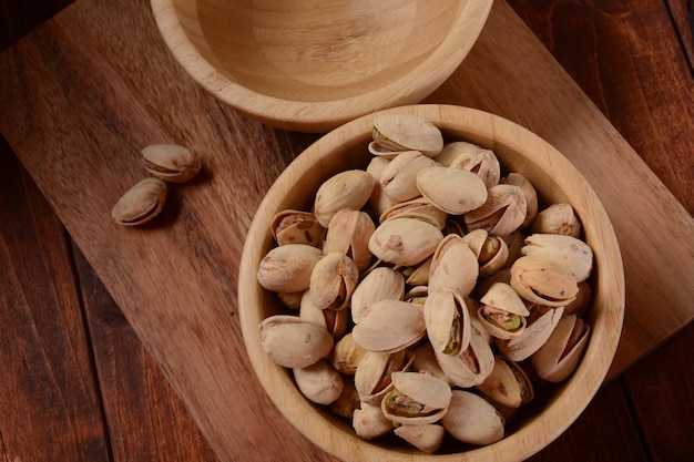 Pistacchi in una ciotola di legno sulla superficie di legno mucchio di pistacchi pistacchi tostati in una ciotola