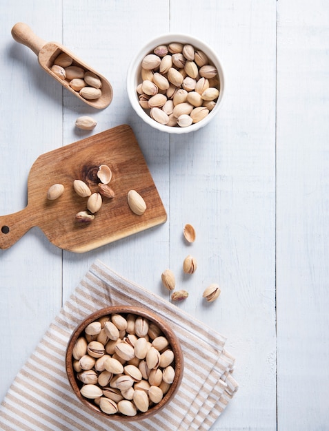 Pistacchi piatti in ciotole, su un tagliere e in un cucchiaio su un fondo di legno bianco. Cibo sano e vegano. Vista dall'alto e copia immagine dello spazio