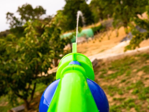 Pistola ad acqua che spara in prima persona una dispersione d'acqua verso il giardino al tramonto e le montagne sullo sfondo