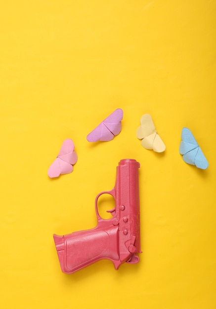 Pistola rosa con farfalle origami su sfondo giallo Concetto creativo Minimalismo Disposizione piatta Disposizione minima Vista dall'alto