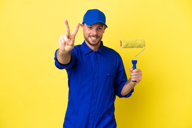 Pittore brasiliano uomo isolato su sfondo giallo sorridente e mostrando segno di vittoria