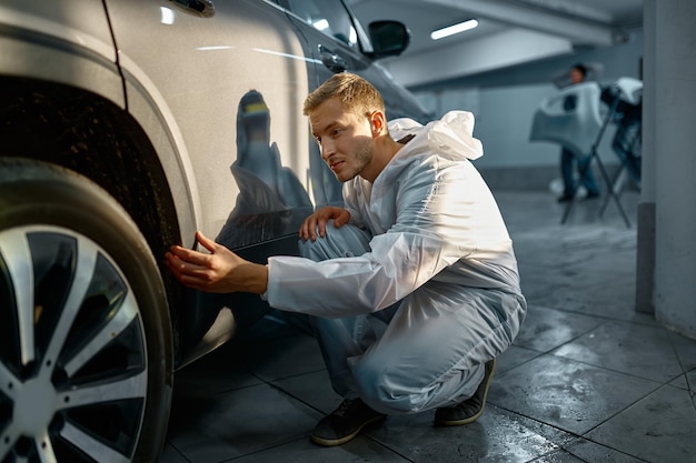 Pittore che esamina la vernice della carrozzeria. Uomo che analizza il valore del danno sulla superficie dell'automobile