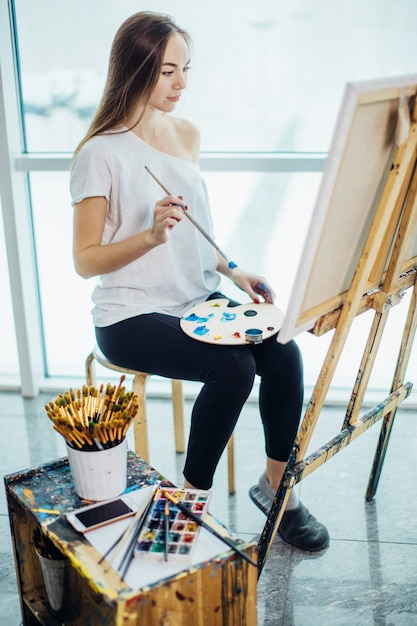 Pittore, ragazza europea che disegna paesaggi marini su tela nel suo laboratorio. Concetto di lezioni di belle arti