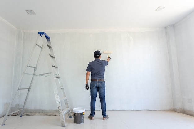 Pittore uomo al lavoro con un rullo di vernice sul muro