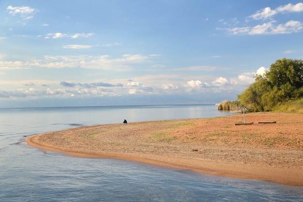 Pittoresca riva del lago di sabbia con cielo azzurro e nuvole in una giornata estiva.