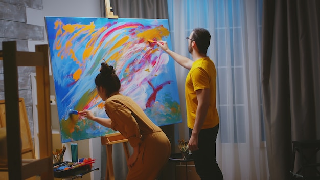 Pittori uomo e donna che lavorano insieme in studio d'arte su tela di grandi dimensioni.