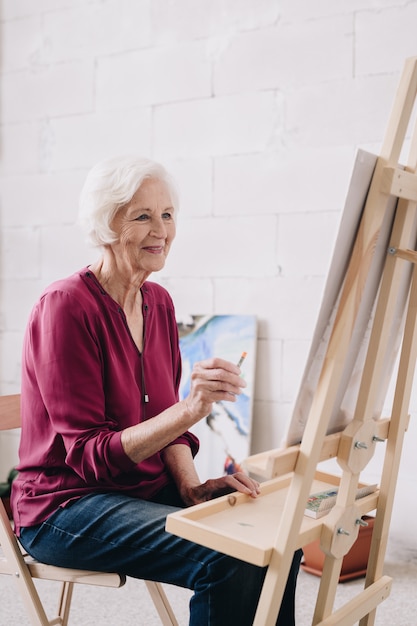 Pittura senior sorridente della donna al cavalletto