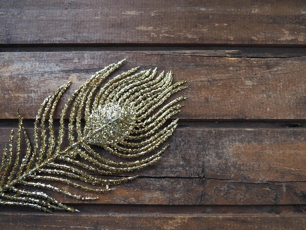 Piuma di pavone dorata. Ramo dorato decorativo a forma di coda e occhiello di pavone. Fondo in legno. Decorazione festiva e bellissimo arredamento di carnevale. Spazio di copia piatto