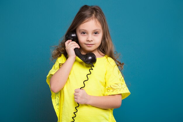 Piuttosto, bambina in t-shirt con capelli castani tenere il telefono