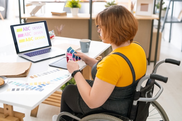 Piuttosto giovane designer di abbigliamento casual seduto sul posto di lavoro in ambiente domestico e scegliendo il colore per il design del sito Web dalla tavolozza