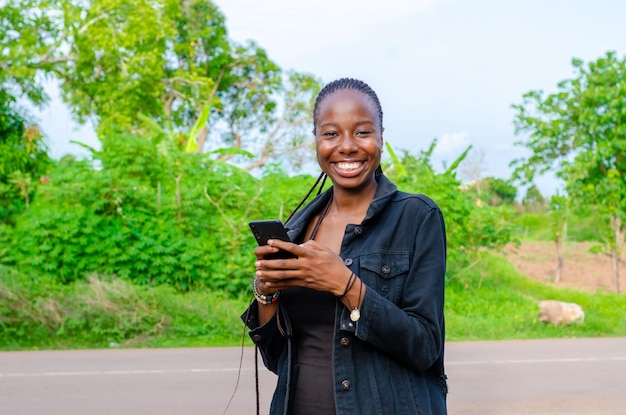 Piuttosto giovane donna africana sorridente e utilizzando il suo telefono cellulare all'aperto