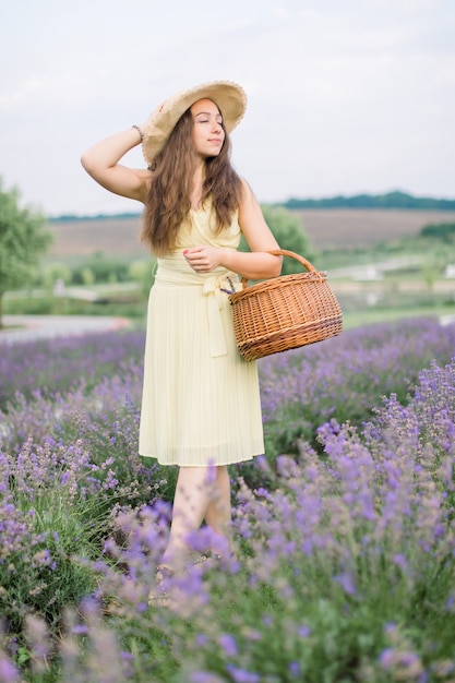Piuttosto giovane donna, camminando con la borsa di vimini nel campo di lavanda in fiore estivo