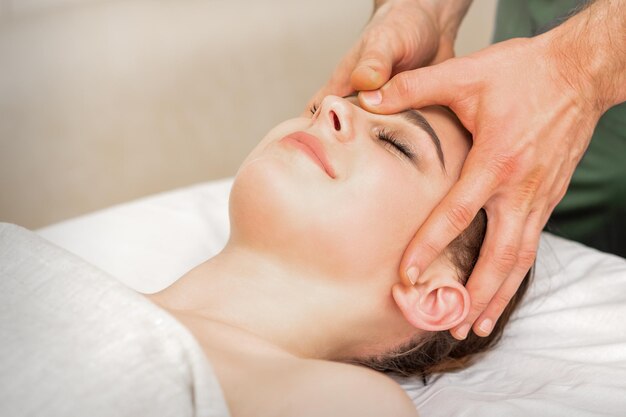 Piuttosto giovane donna caucasica che riceve un massaggio alla testa da un massaggiatore maschio in un salone di bellezza.