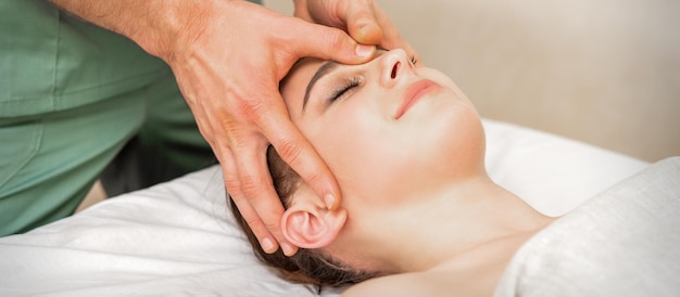 Piuttosto giovane donna caucasica che riceve un massaggio alla testa da un massaggiatore maschio in un salone di bellezza.