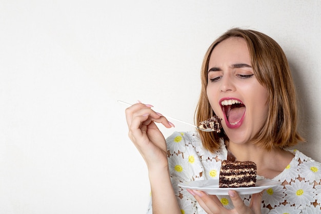 Piuttosto giovane donna che mangia una gustosa torta al cioccolato su sfondo bianco. Spazio per il testo