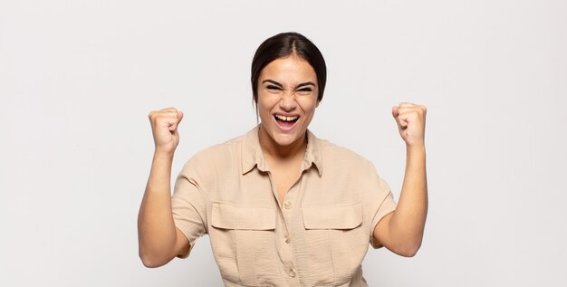 Piuttosto giovane donna che si sente felice, sorpresa e orgogliosa, gridando e celebrando il successo con un grande sorriso