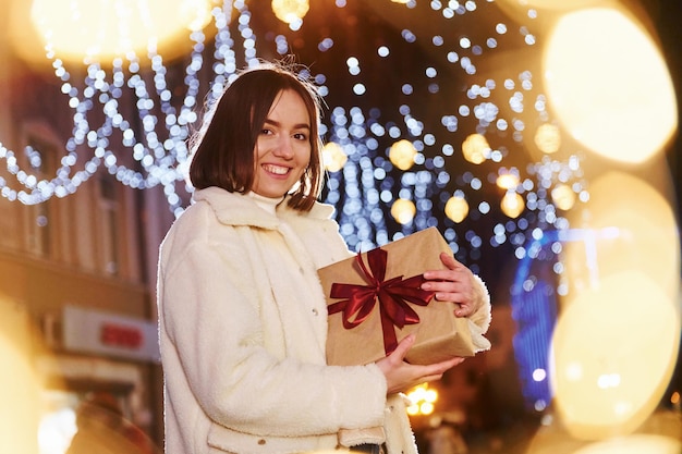 Piuttosto giovane donna con confezione regalo in piedi all'aperto sulla strada