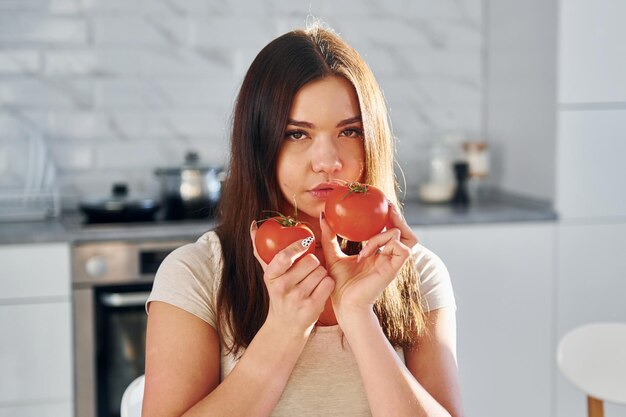 Piuttosto giovane donna in abiti casual si siede sulla cucina con i pomodori