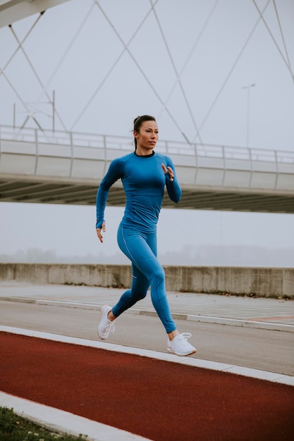 Piuttosto giovane donna in tuta blu che corre lungo il fiume al mattino d'autunno