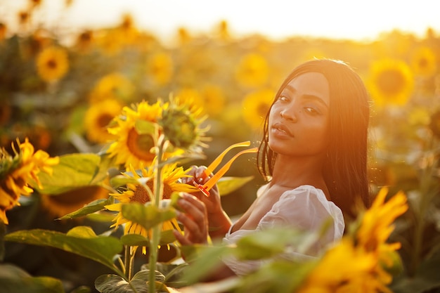 Piuttosto giovane donna nera indossare abito estivo posa in un campo di girasoli.