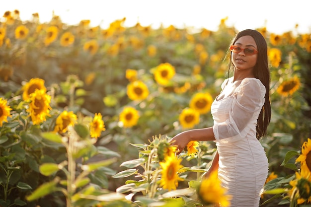 Piuttosto giovane donna nera indossare abito estivo posa in un campo di girasoli