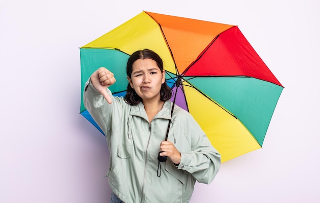 Piuttosto giovane donna sentirsi croce, mostrando i pollici verso il basso. concetto di pioggia e ombrello