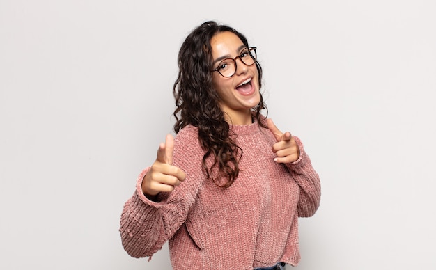 Piuttosto giovane donna sorridente con un atteggiamento positivo, di successo, felice che punta alla telecamera, facendo segno di pistola con le mani