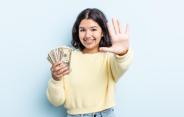 Piuttosto giovane donna sorridente e dall'aspetto amichevole, mostrando il numero cinque. concetto di banconote in dollari