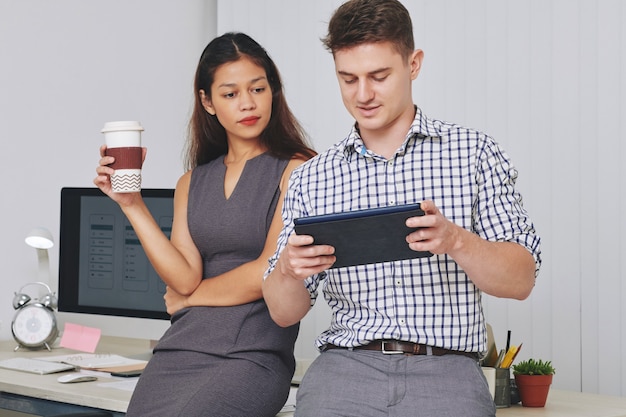 Piuttosto giovane imprenditrice di razza mista che beve caffè e guardando lo schermo su tablet PC nelle mani del suo collega