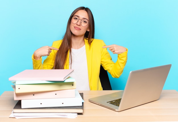 Piuttosto giovane imprenditrice guardando orgoglioso, positivo e casual che punta al petto con entrambe le mani